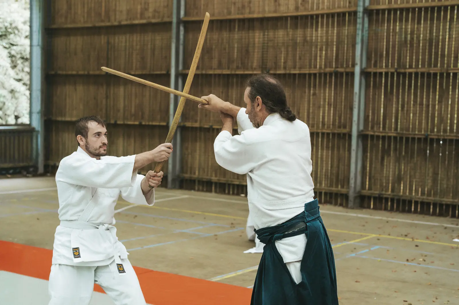 Deux pratiquants s’affrontent au bokken dans la salle du dojo