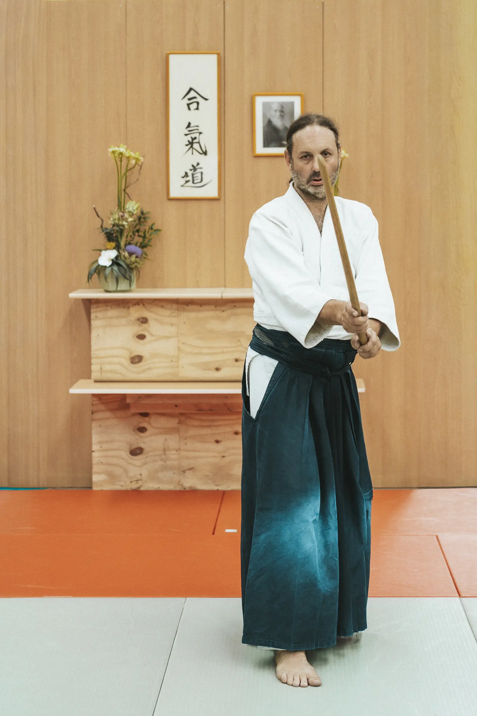 Michaël Ameye, professeur du Suu Dojo, se tient droit au tatami avec son bokken devant une calligraphie