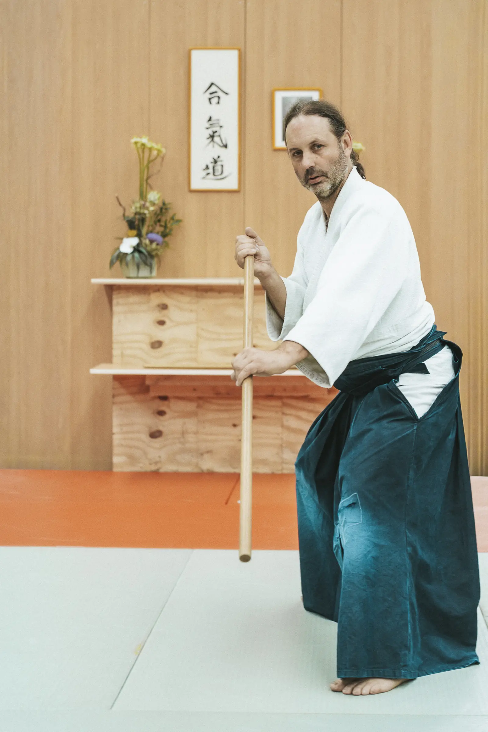 Le professeur se tient en garde, bokken pointé vers le sol, devant l’alcôve du dojo
