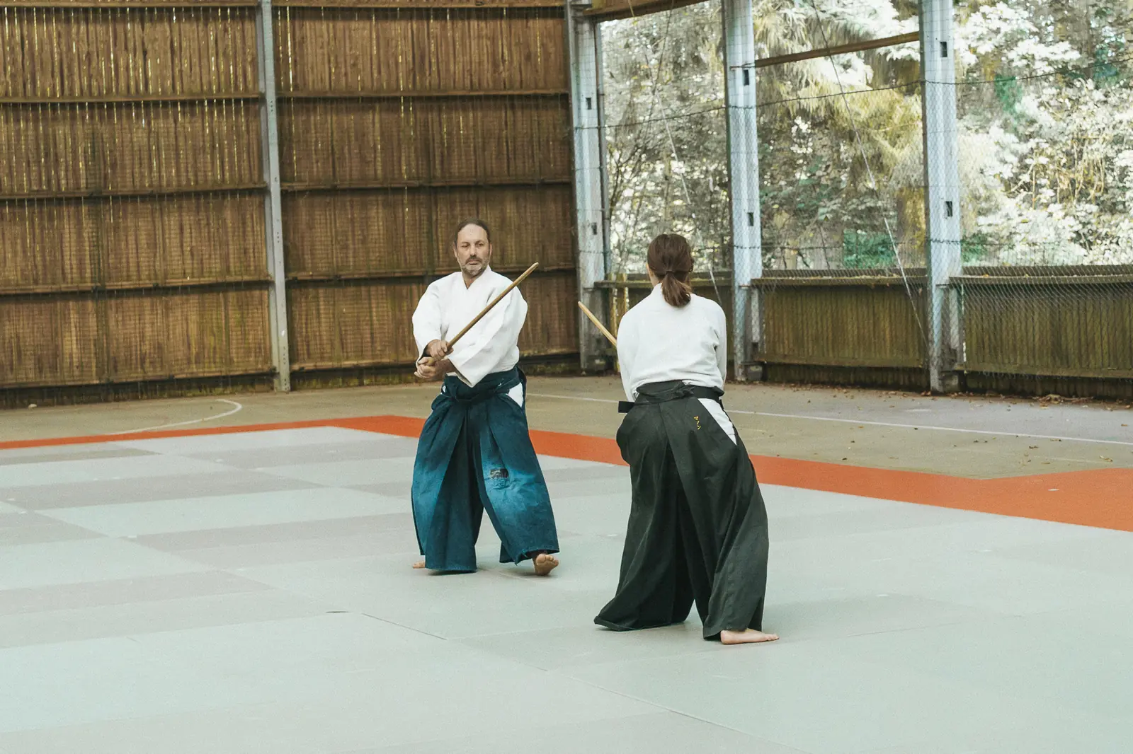 Deux pratiquants au bokken sur le tatami, au fond de la salle